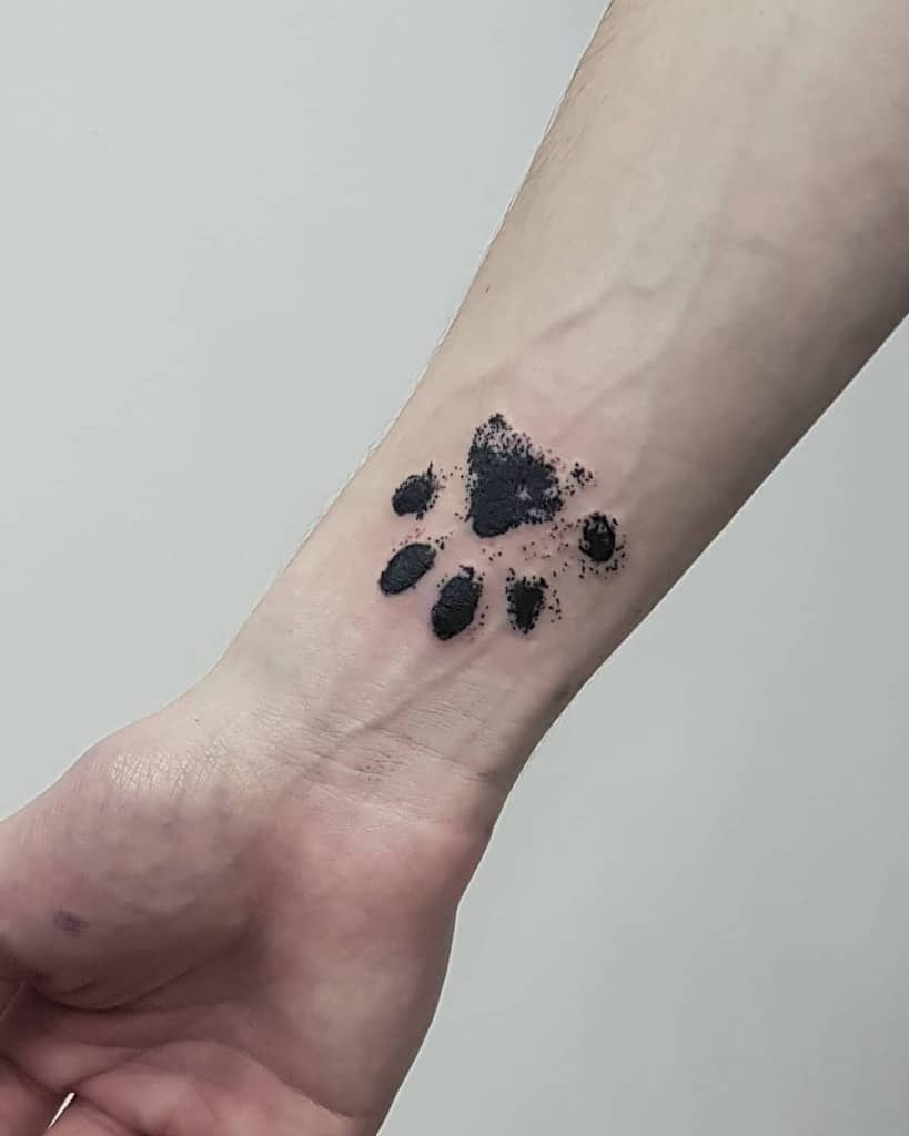 Tattoo of a black cat paw print on a person's inner wrist