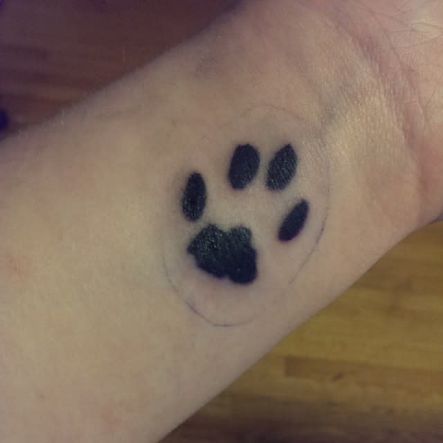 A tattoo of a black cat paw print on a person's wrist