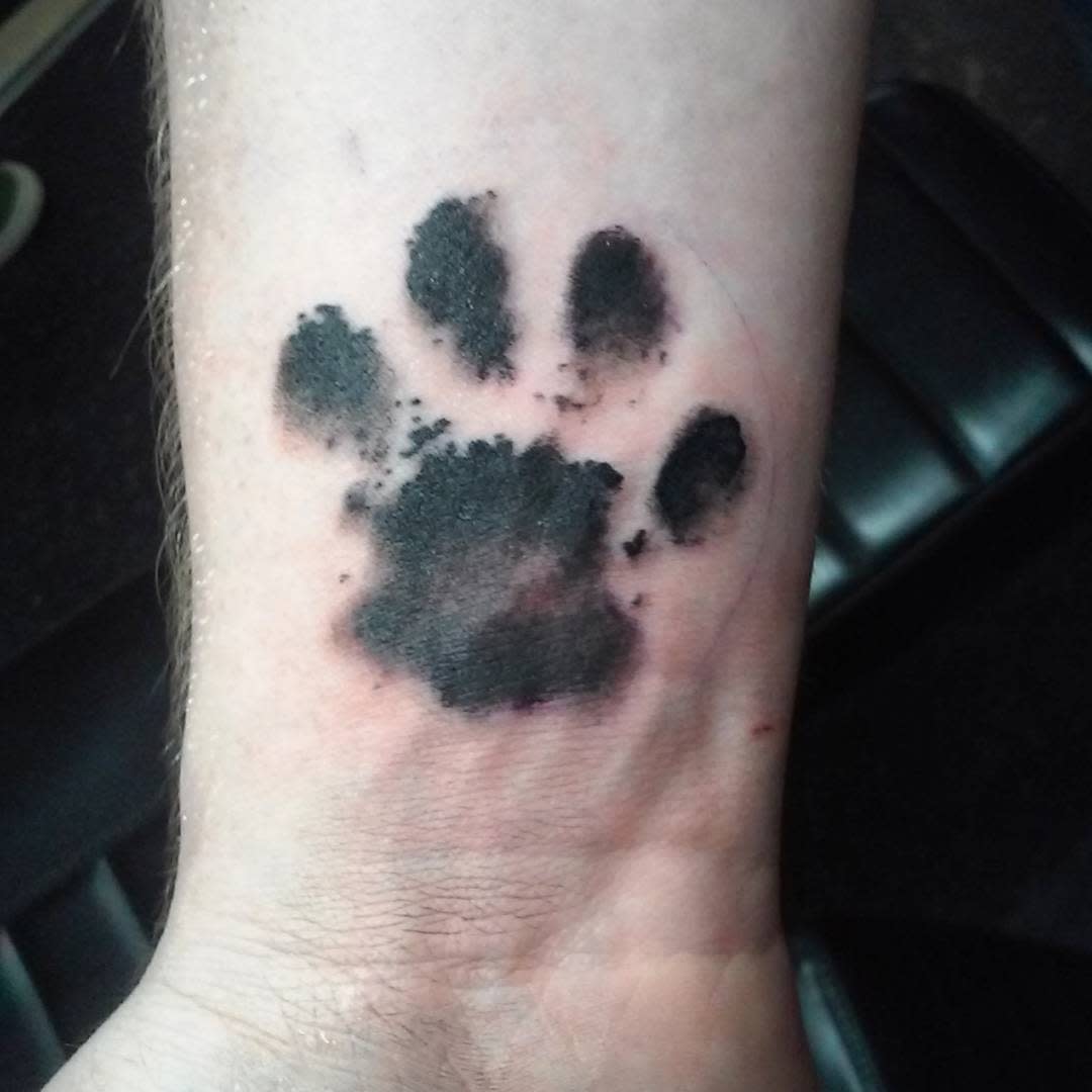 Forearm tattoo of a black cat paw print with slight fading, placed just above the wrist