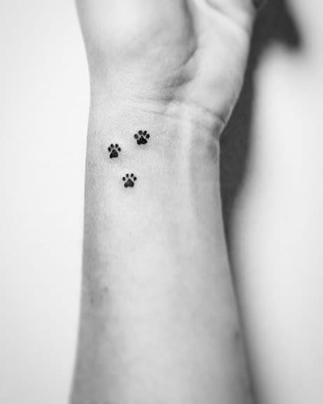 Black and white tattoo of three small paw prints on the inside of a person's wrist