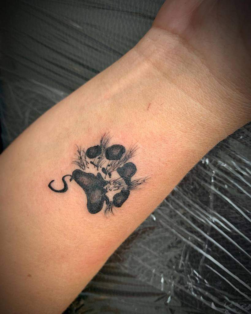 Black paw print tattoo with small heart details and shading on an arm