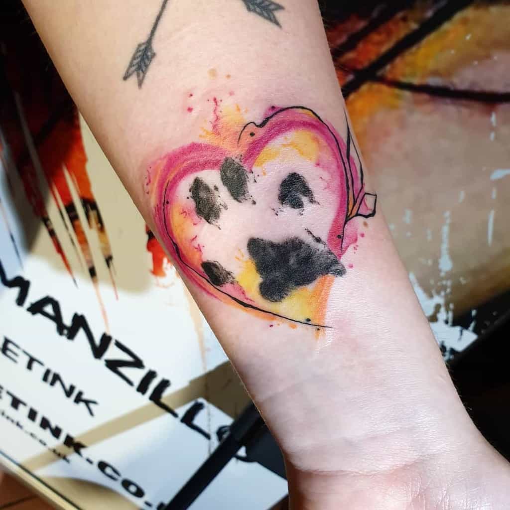 Tattoo of a black cat paw print within a colorful heart on a forearm
