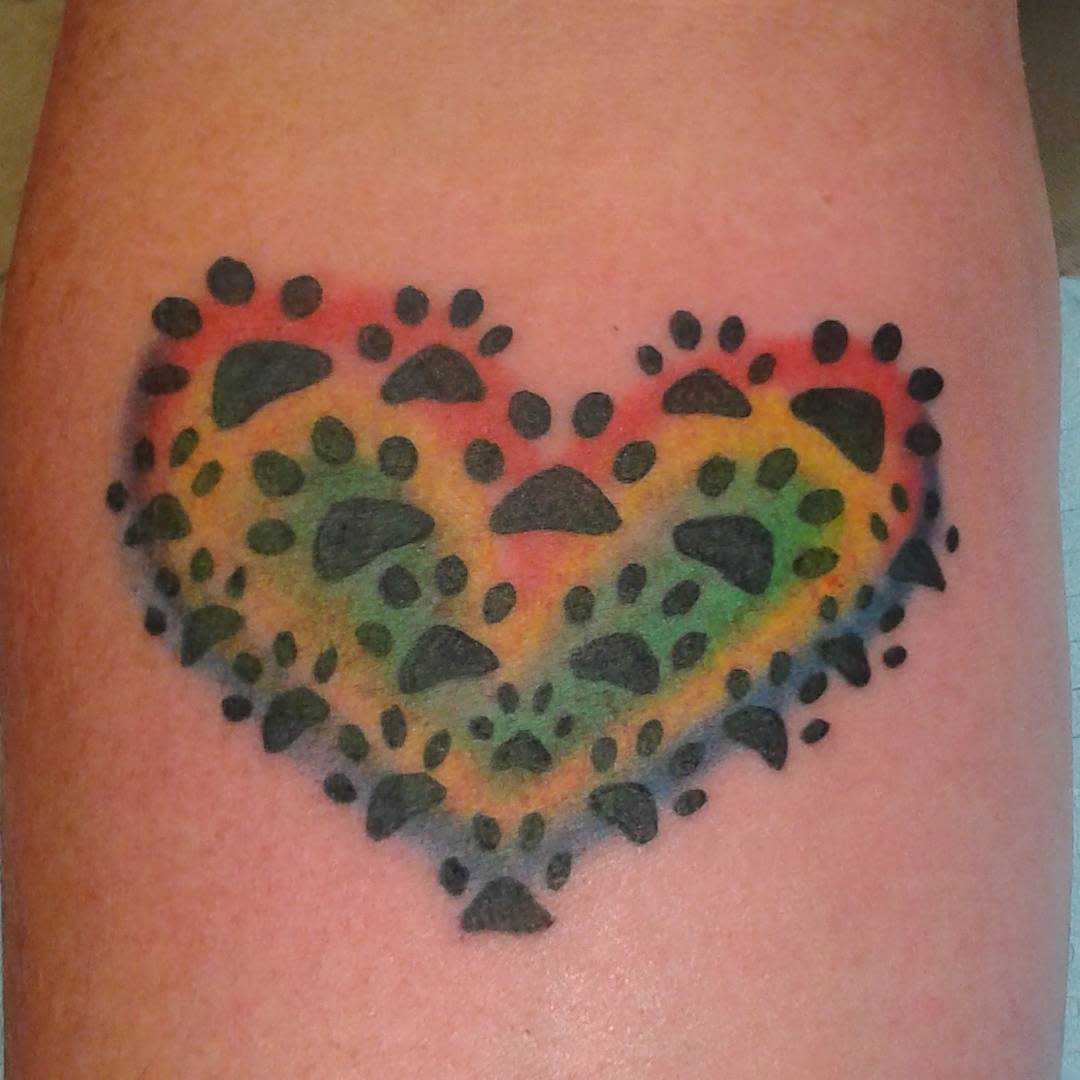 A tattoo of a heart made from black cat paw prints with a rainbow background
