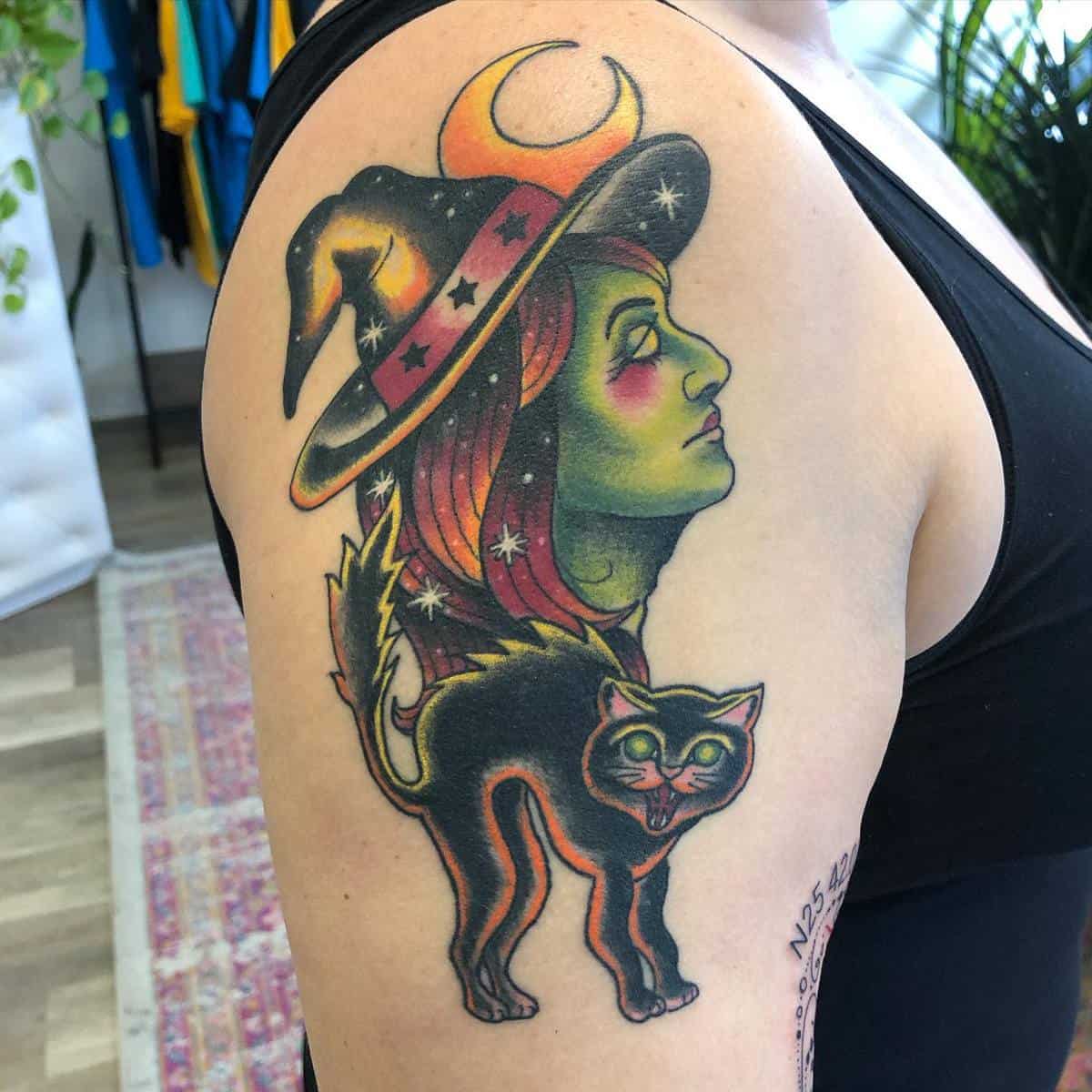 Tattoo of a green-skinned witch wearing a hat with a black cat and crescent moon on the arm