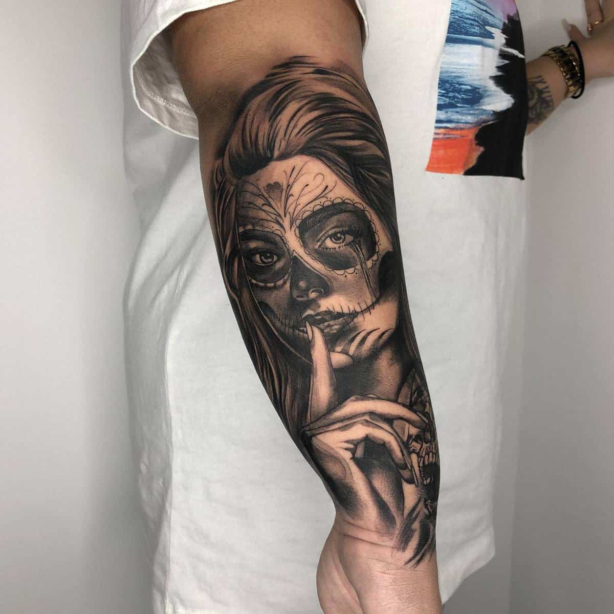 Black-and-grey forearm tattoo of a woman with Catrina face paint, symbolizing silence and mystery