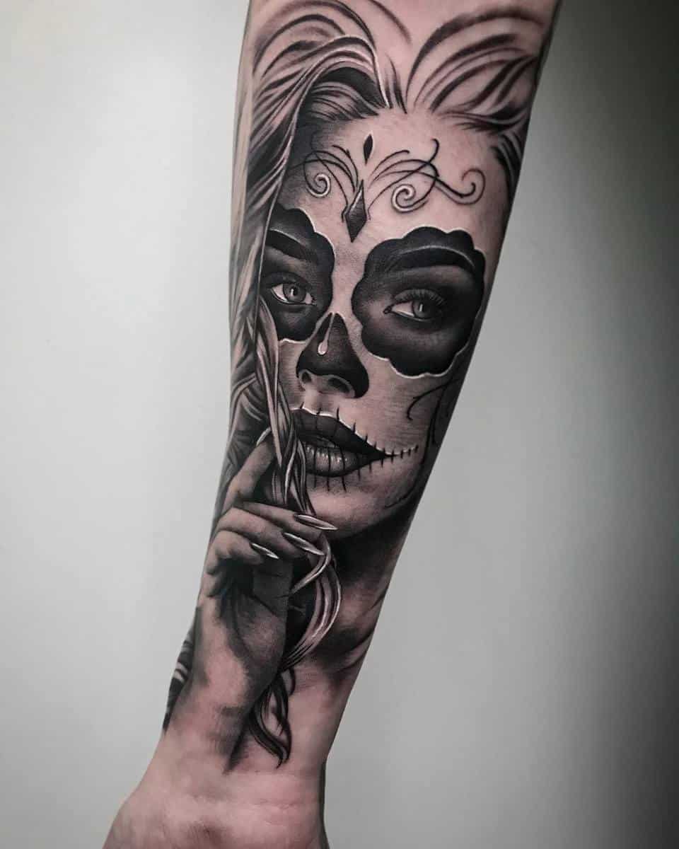 Forearm tattoo of a woman with Catrina face paint, holding a finger to her lips, symbolizing silence