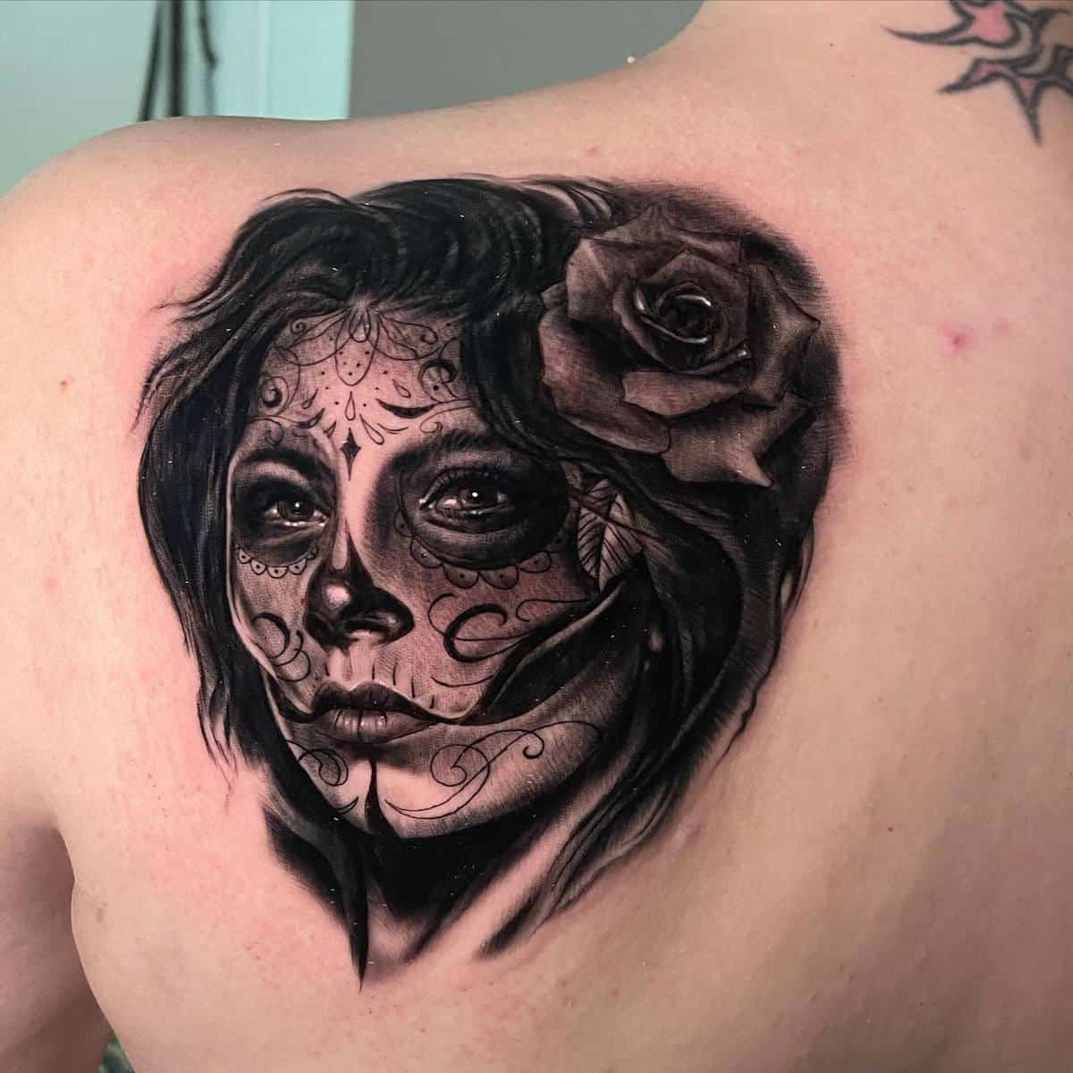 Black-and-grey Catrina tattoo on the upper back, with delicate face paint and a large rose on her head