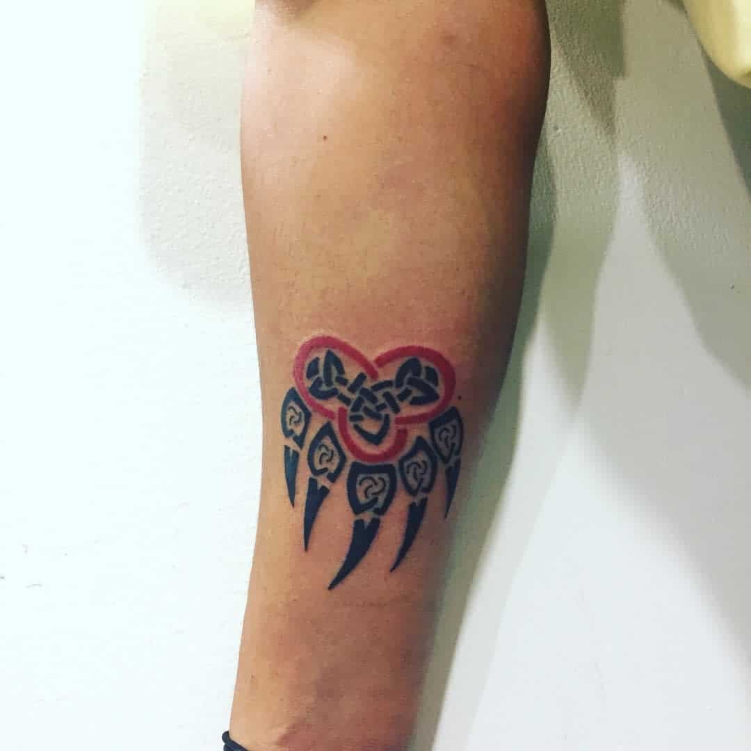 Arm tattoo of a red and black dreamcatcher-inspired design with five feather-like elements, accented by a subtle bear paw