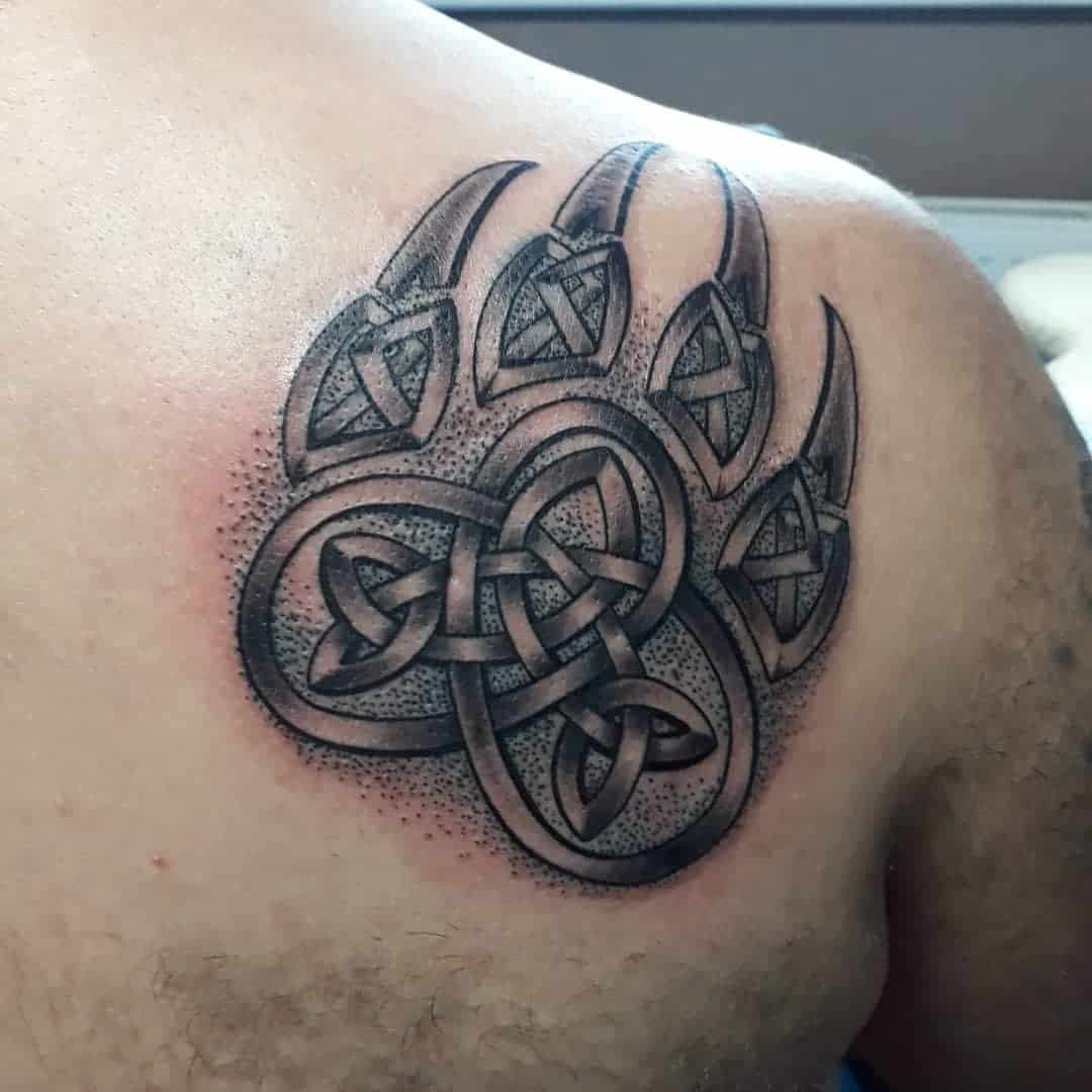 Tattoo of a bear paw intricately designed with Celtic knots, beautifully placed on a person's shoulder