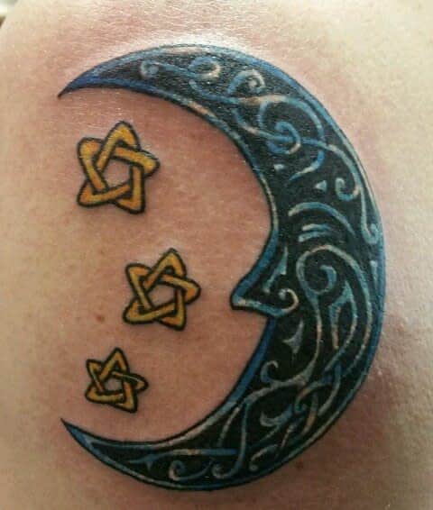 Tattoo of a blue crescent moon with intricate patterns and three yellow Celtic knots