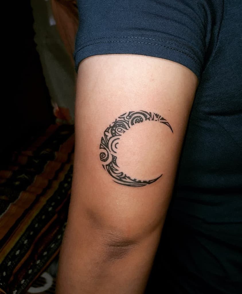 An arm with an intricately designed crescent moon tattoo in deep black ink