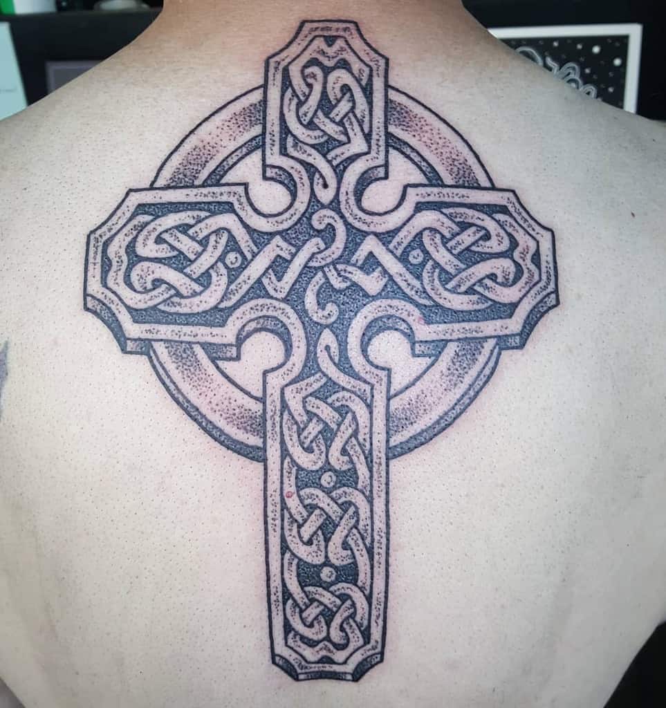 A large Celtic cross tattoo on the upper back, featuring detailed knotwork and dot shading, creating a bold and intricate design
