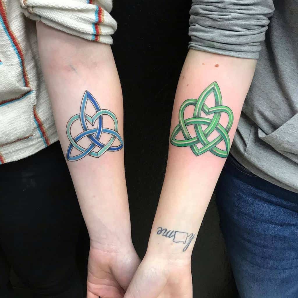 Two forearms with matching Celtic knot tattoos, one in blue and the other in green
