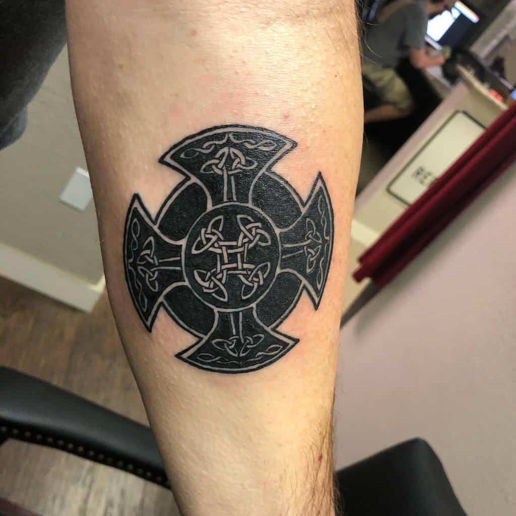 Black ink Scottish Celtic cross tattoo with detailed knotwork inside a circular centerpiece and triquetra designs in each arm of the cross