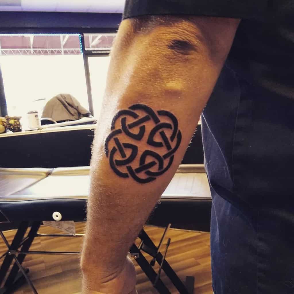 A black Scottish Celtic knot tattoo with four interwoven loops forming a symmetrical circular pattern with bold, solid lines.