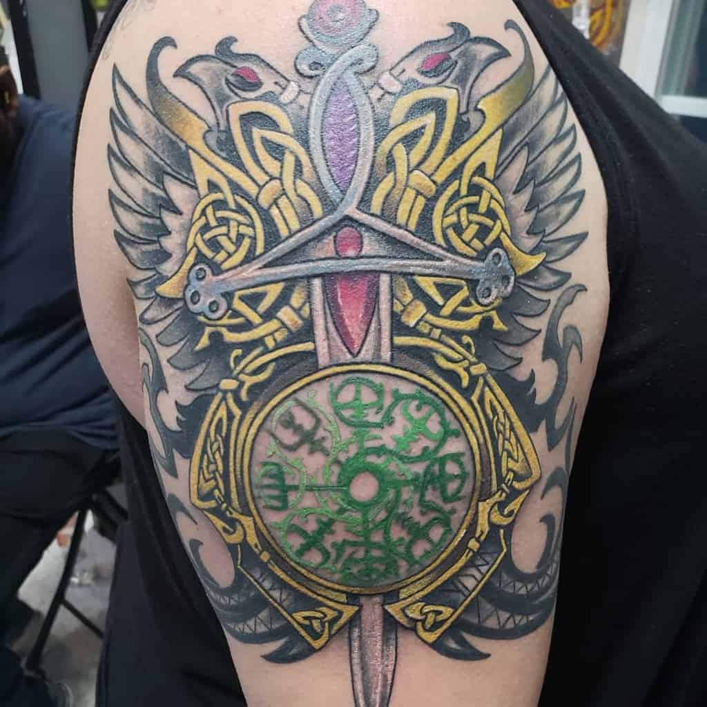 Intricate Scottish tattoo of a sword flanked by wings, Celtic knots, gold detailing, and a green circular design with mystical symbols