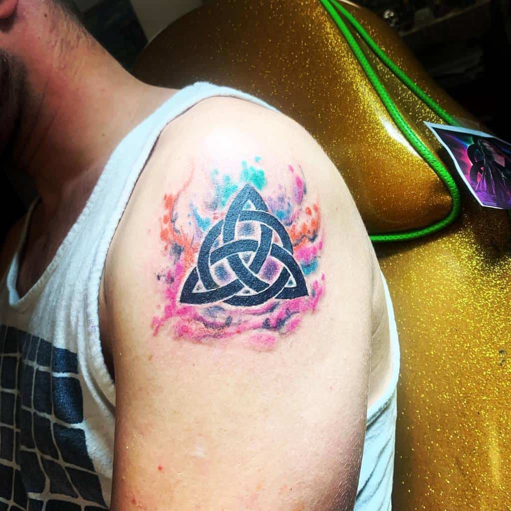 A black Scottish Celtic triquetra tattoo, surrounded by a watercolor splash of blue, pink, and orange hues