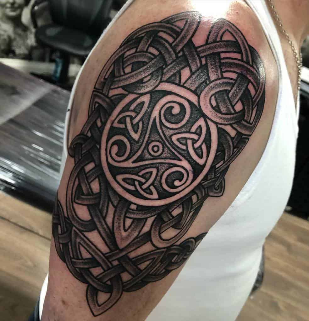 An intricate black and grey Scottish Celtic knot tattoo, featuring a central triskelion within a circular frame