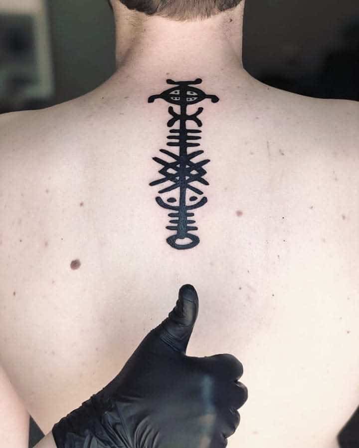 A black Celtic tribal tattoo running vertically along the spine, featuring intricate knotwork and symbolic shapes