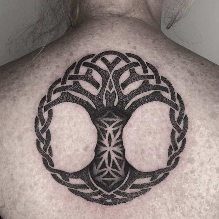 A detailed black Celtic tree of life tattoo on the upper back, featuring intricate knotwork within the tree's branches and roots