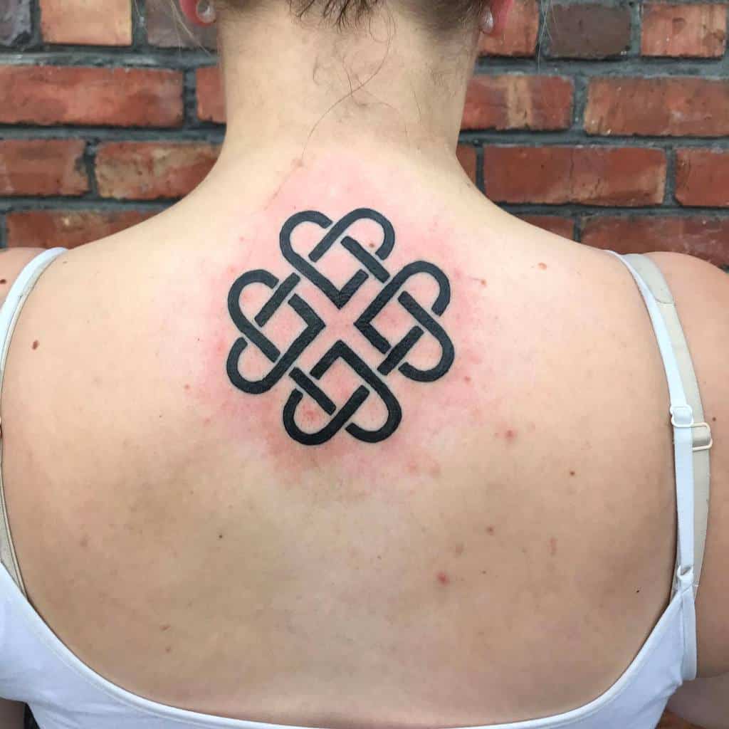 A bold black Celtic knot tattoo on the upper back, featuring an intricate, interwoven loop pattern symbolizing eternity