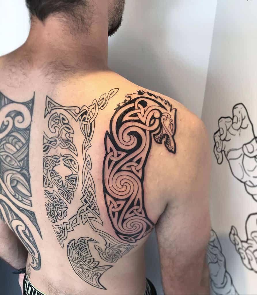 A Celtic-inspired tattoo on the upper back and shoulder featuring a stylized black wolf design with intricate knotwork and tribal patterns