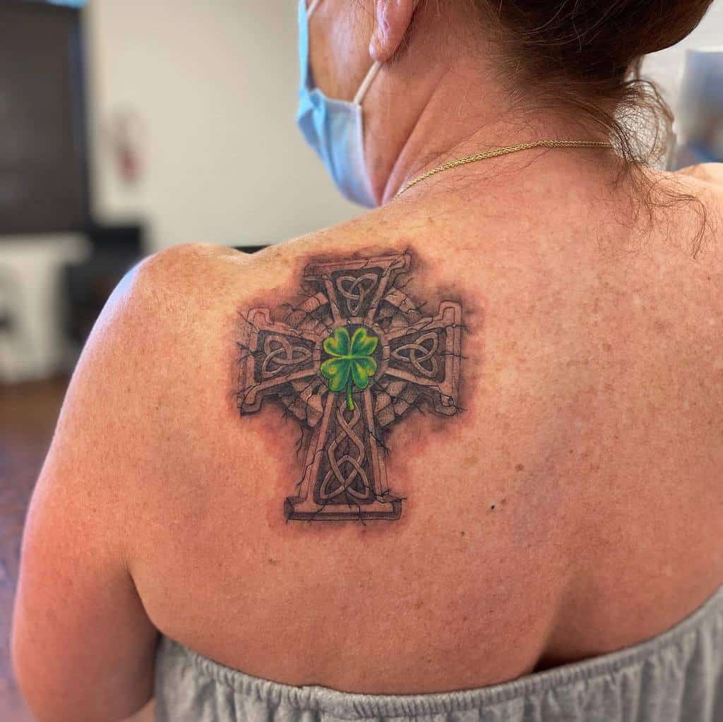 A woman with a Celtic cross tattoo featuring a green shamrock on her shoulder