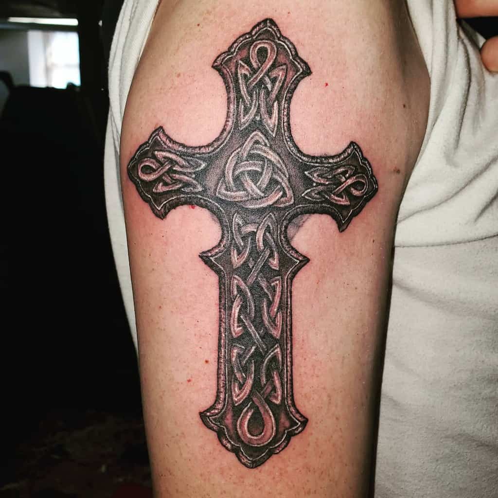 Tattoo of an ornate Celtic cross with intricate knotwork elegantly wrapped around the upper arm