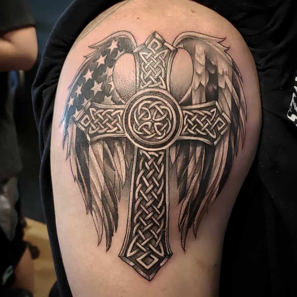 Tattoo of a Celtic cross with wings, featuring intricate details of the American flag on an upper arm