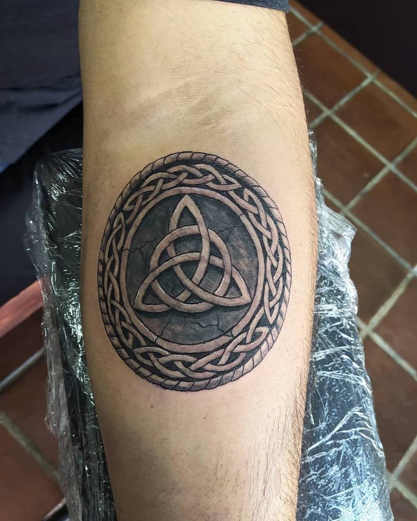 Tattoo of a Celtic trinity knot with a circular braided border on an arm