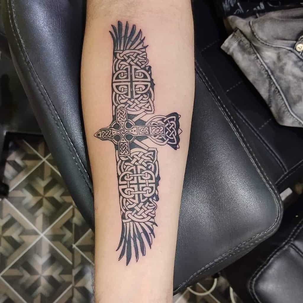 Forearm tattoo of a bird with intricate, dark Celtic knotwork designs and spread wings