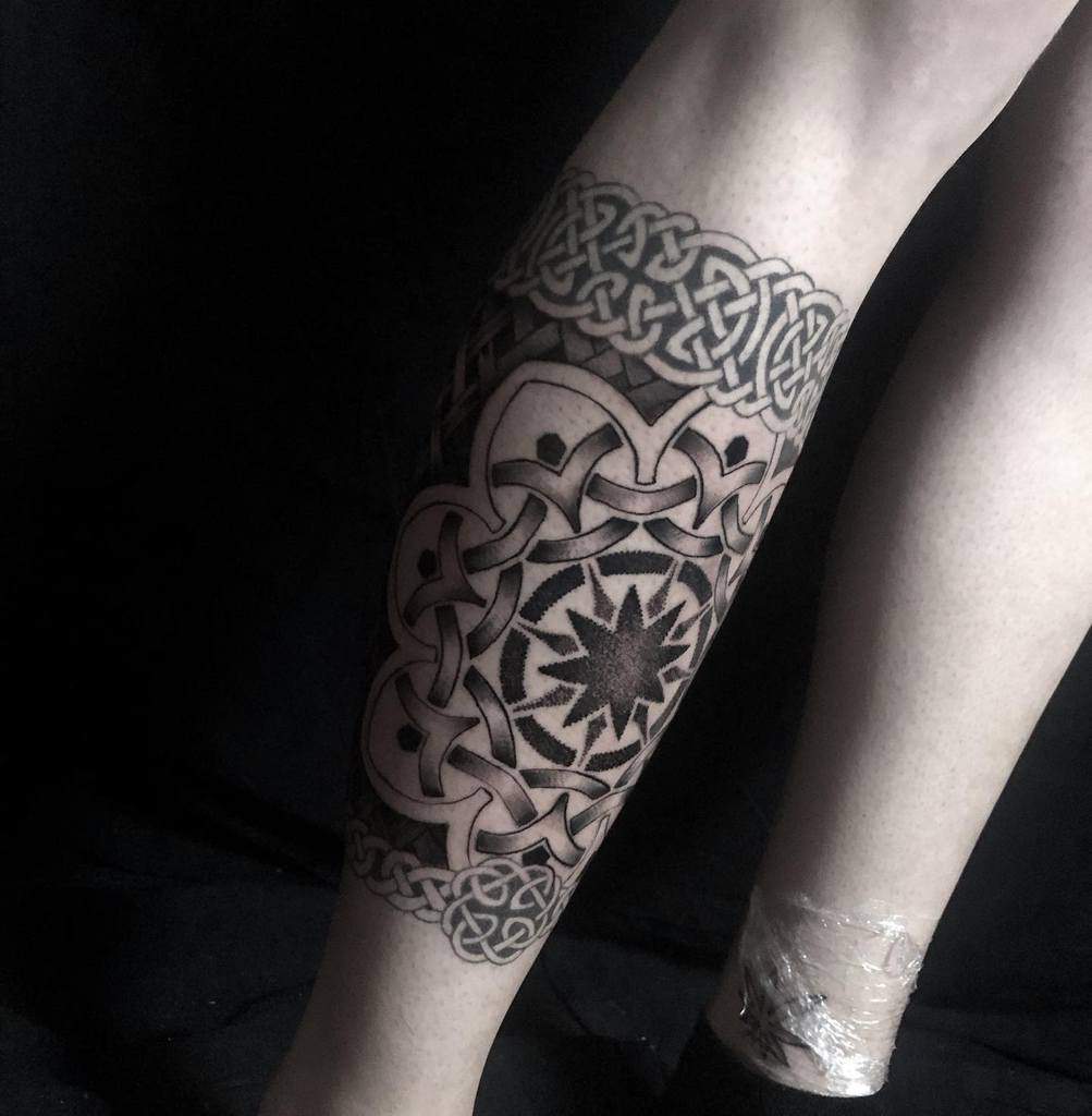 A detailed leg tattoo featuring Celtic knotwork bands and a central geometric star pattern, creating a bold and intricate design