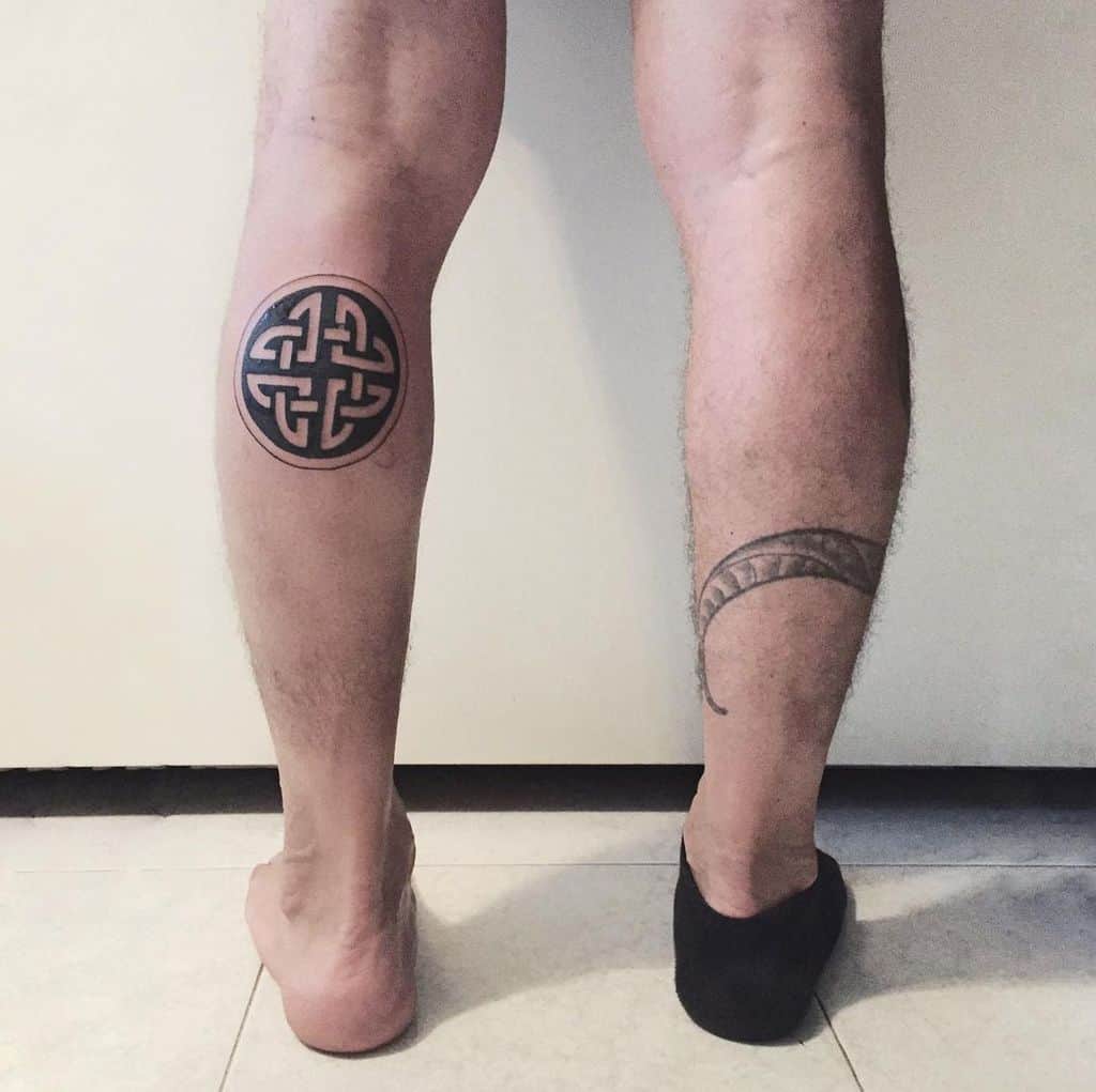 A simple black Celtic knot tattoo on the back of the left calf, featuring a circular design, with a separate crescent moon tattoo on the right calf