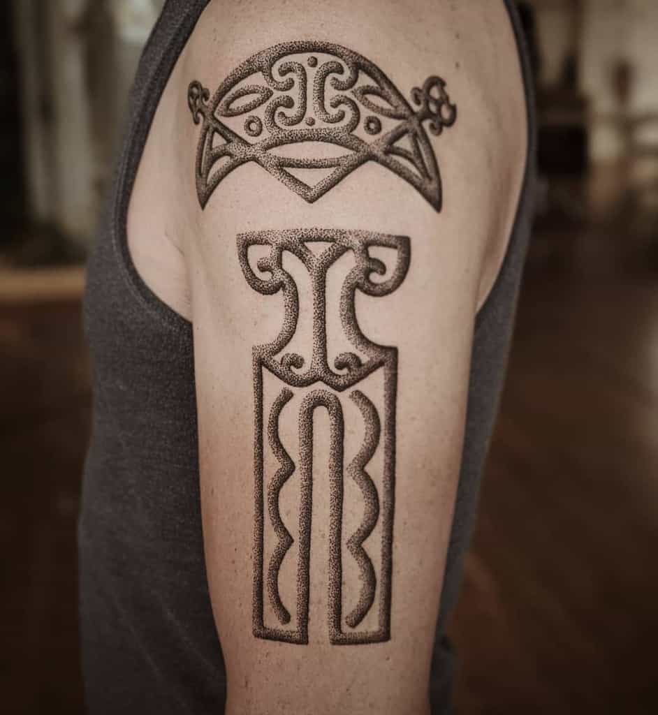 A geometric Celtic-inspired tattoo on the upper arm, featuring bold dotwork patterns and abstract knotwork