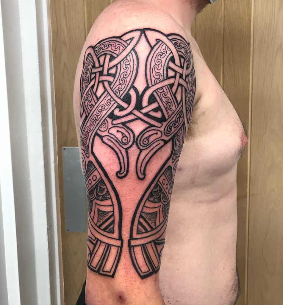 A bold Celtic-inspired upper arm tattoo featuring intricate knotwork, symmetrical patterns, and strong black outlines