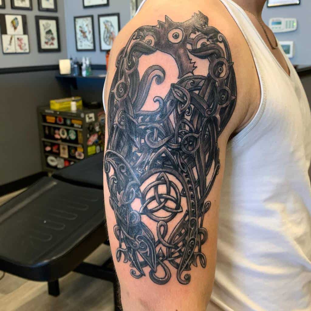 A detailed Celtic-inspired upper arm tattoo featuring intricate knotwork, swirling patterns, and bold linework, incorporating a central triquetra symbol