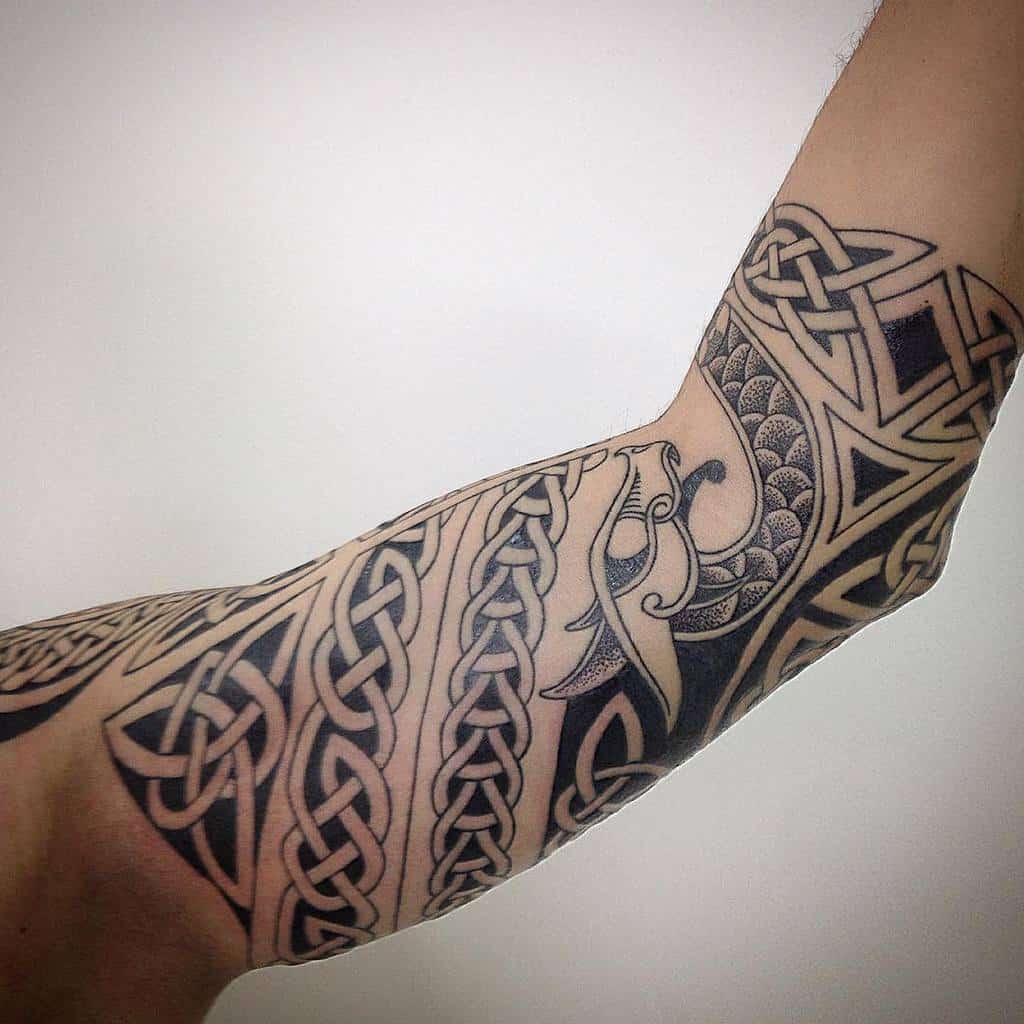 Arm tattoo with intricate black Celtic knots and Norse design, featuring complex geometric and animal patterns