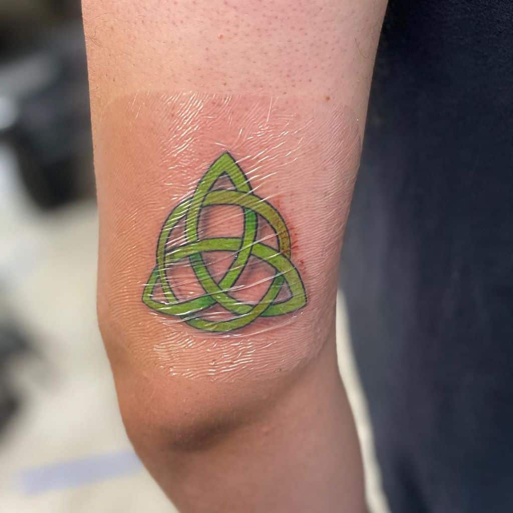 A green Celtic triquetra tattoo on a person's elbow