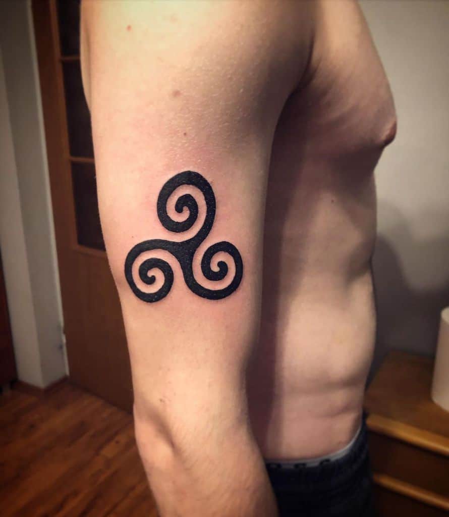 Upper arm tattoo of a black triskelion symbol with three spirals