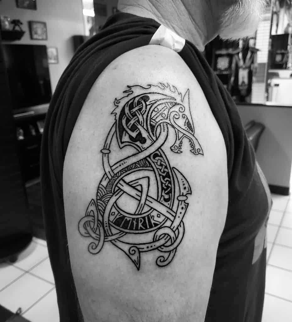 Black and white tattoo of a Viking dragon with tribal patterns on a man's upper arm