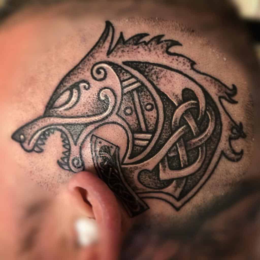 Tattoo of a stylized wolf head with intricate Celtic knot patterns on a shaved head