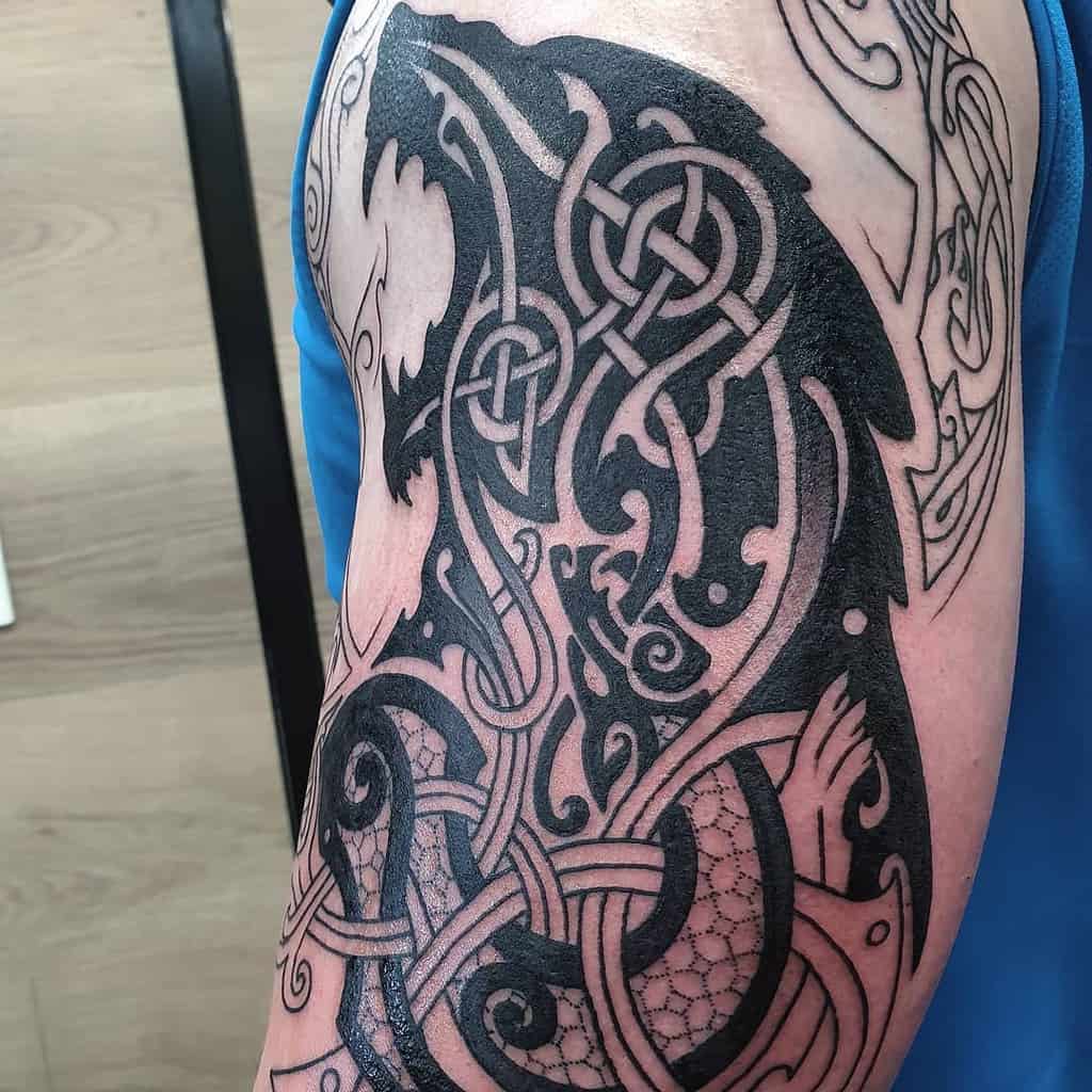 Arm tattoo featuring intricate black tribal designs with wolf motifs and Celtic knots