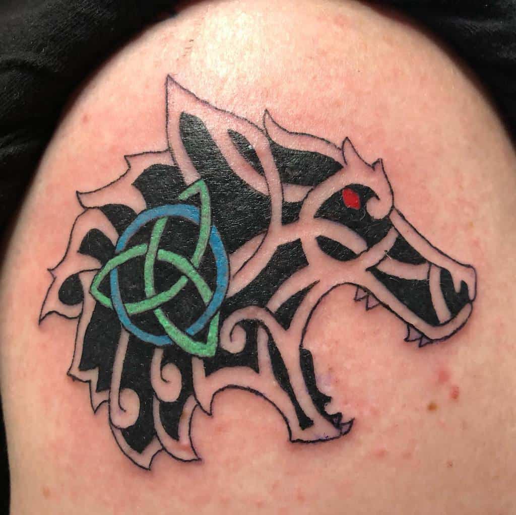 Tattoo of a stylized black wolf head with a green Celtic knot and a red eye