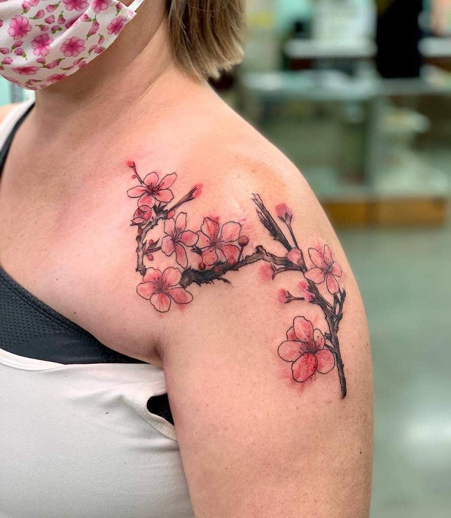A woman with a cherry blossom branch tattoo on their shoulder