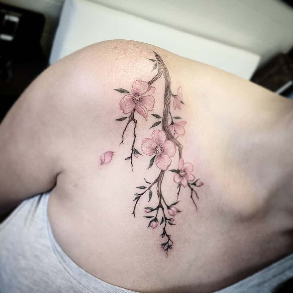 A delicate cherry blossom tattoo adorns a person's shoulder, featuring elegant branches intertwined with soft pink flowers