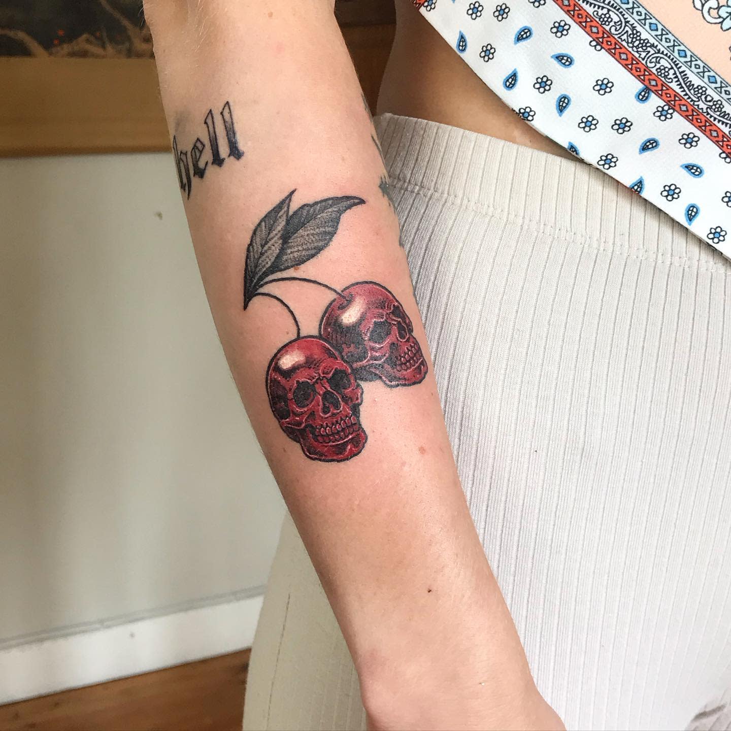 Tattoo of two cherry-shaped skulls on forearm with "hell" tattoo above