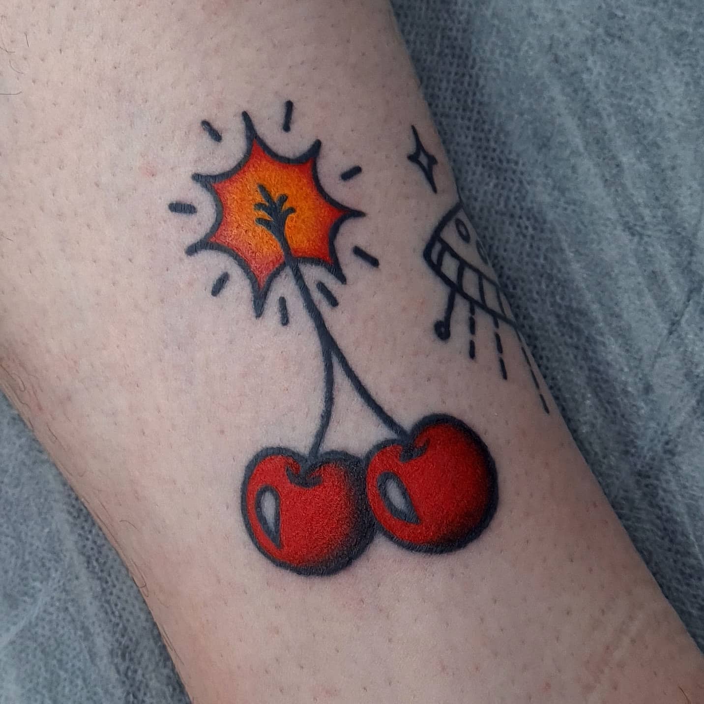 Tattoo of two cherries with a fuse and a small explosion above them