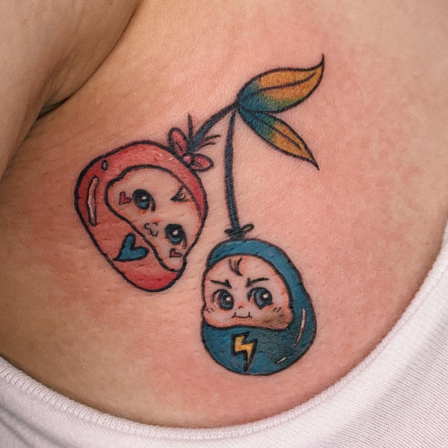 Tattoo of two animated cherries with faces; one red with a heart, one blue with a lightning bolt