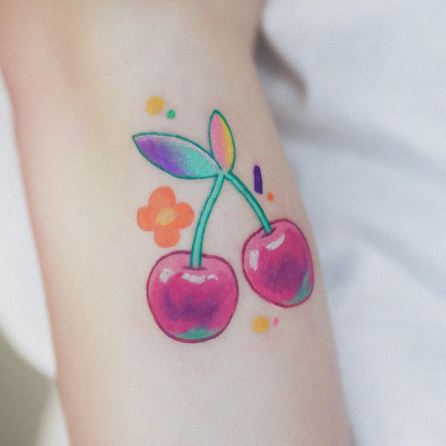 Colorful tattoo of two cherries with leaves and small decorative elements on skin