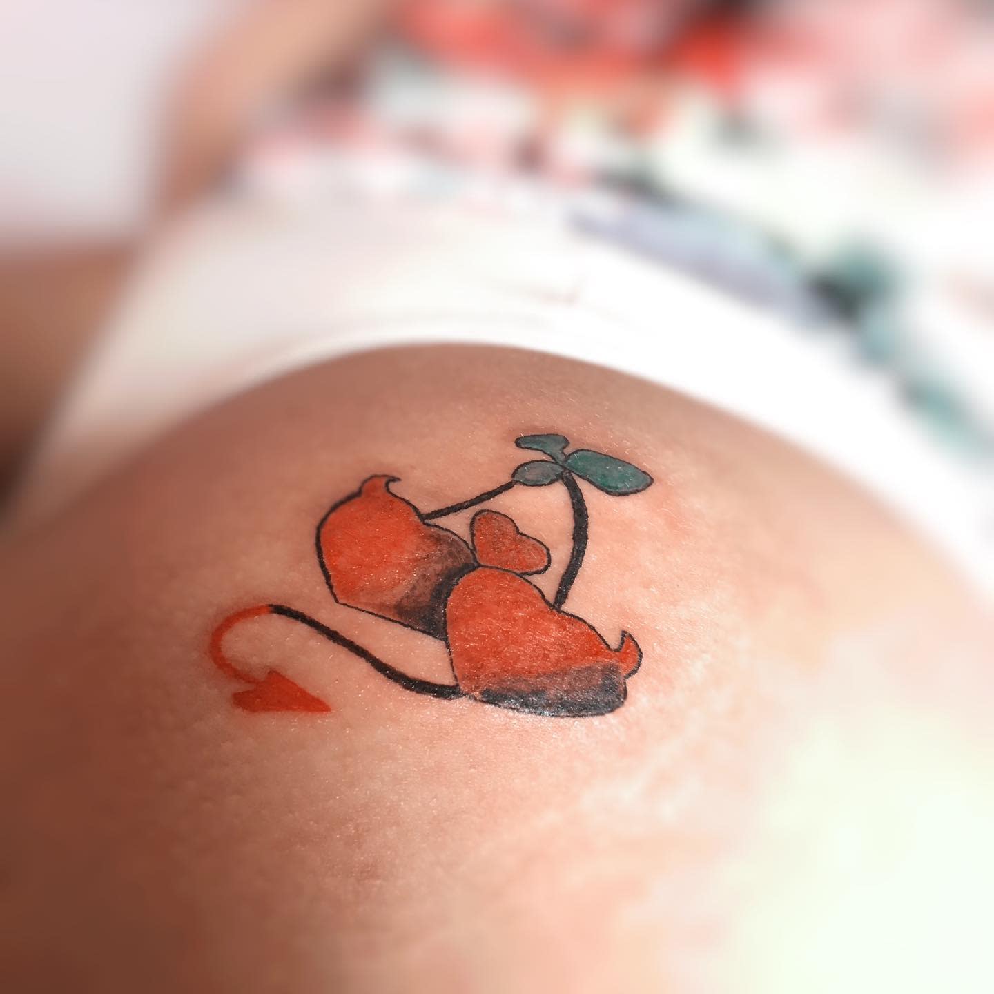 Tattoo of two orange cherries with devil tails and brown stems on light skin